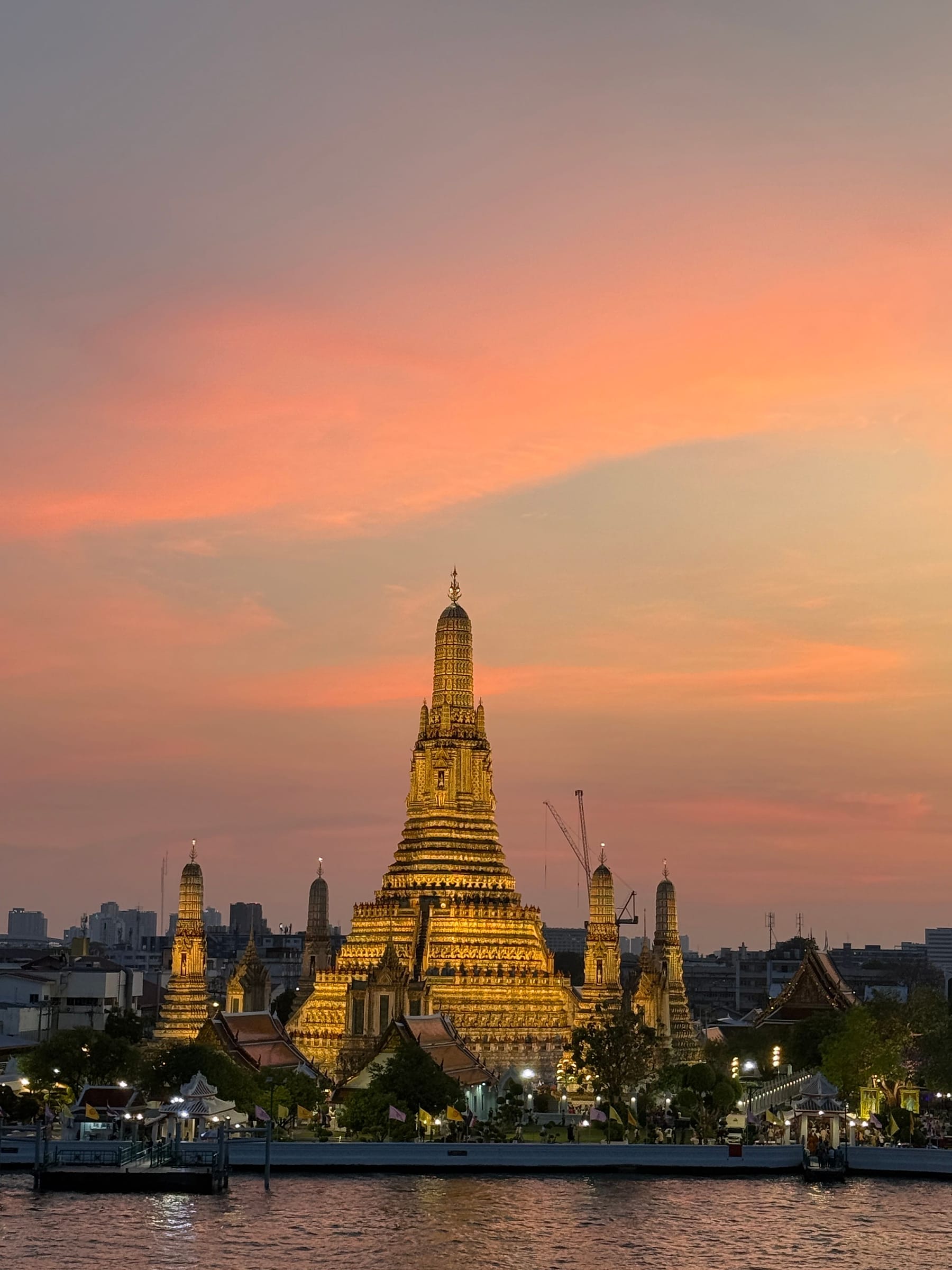 A golden Thai temple spire silhouetted against an orange sunset sky