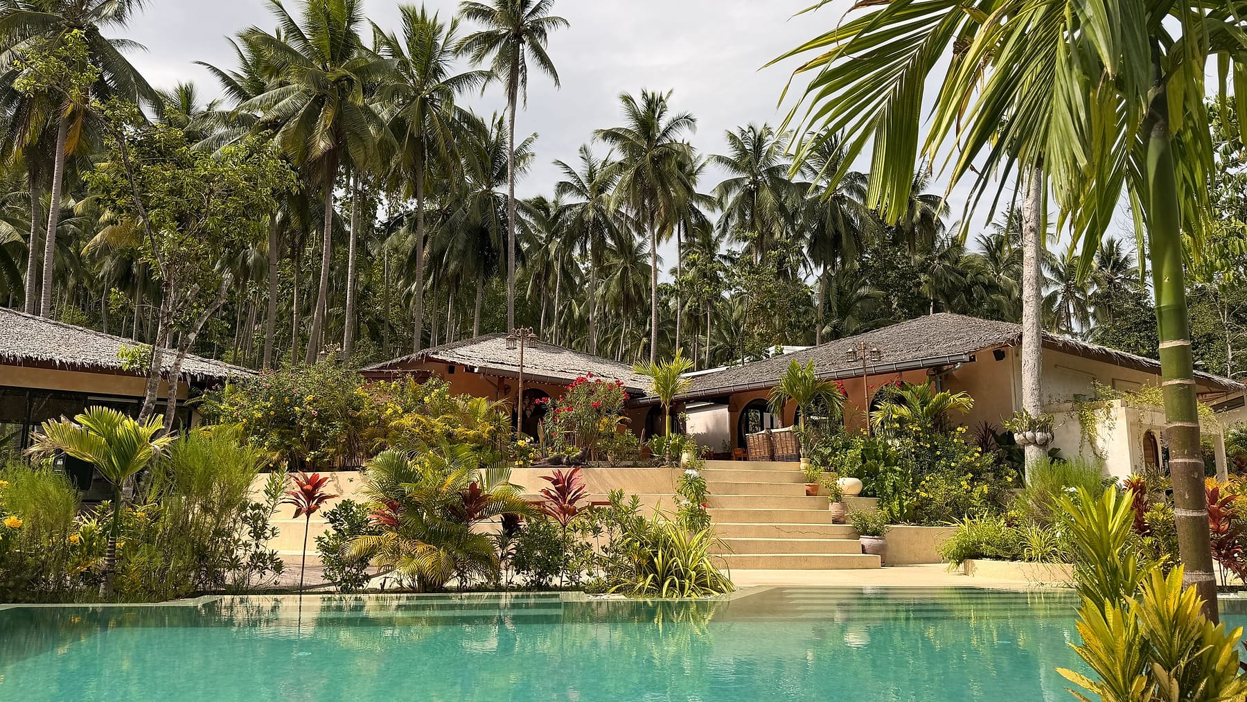 A tropical resort villa with a swimming pool surrounded by tall palm trees in Surat Thani, Thailand