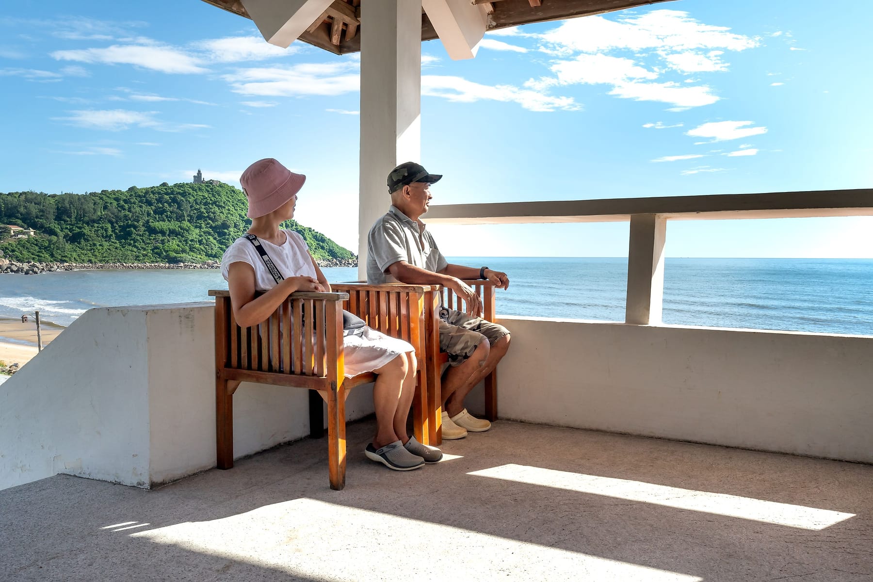 A retired couple sitting together on a shaded balcony looking out over the sea