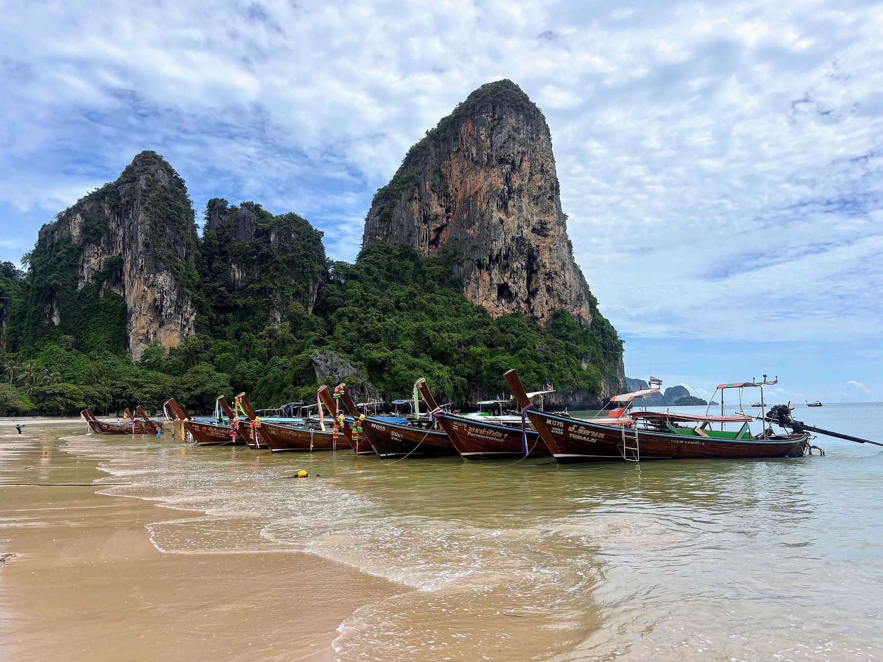 Long-tail boats lined along Railay Beach in Krabi with limestone cliffs behind